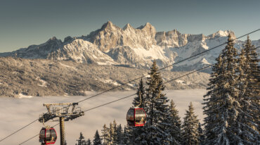 Panorama skischans in Radstadt voor een prachtig winters berglandschap met besneeuwde bomen en twee rode gondels.