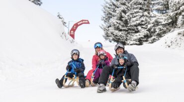 Een familie die rodelplezier heeft, van voren gefotografeerd met lachende gezichten in een mooi winterlandschap.