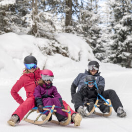 Een familie die rodelplezier heeft, van voren gefotografeerd met lachende gezichten in een mooi winterlandschap.