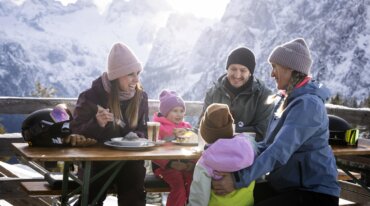 Een familie tijdens de lunch op het zonneterras van een skihut.