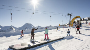 Kinderen leren skiën met de skileraar aan de sleeplift – bij stralend mooi weer en een prachtige winterlandschap.