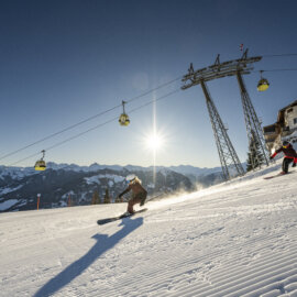 Een skiester die aan het carven is op een perfect geprepareerde piste, met een skiliftgondel op de achtergrond en stralende zonneschijn.