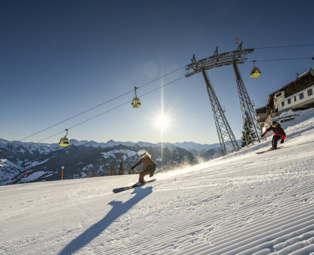 Een skiester die aan het carven is op een perfect geprepareerde piste, met een skiliftgondel op de achtergrond en stralende zonneschijn.