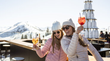 Twee vrouwen genieten in de hut van een glas Aperol en hebben allebei een stralende glimlach op hun gezicht.