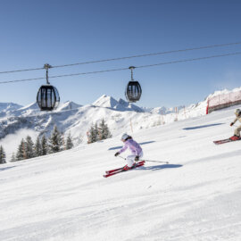 Een skiester die aan het carven is op een perfect geprepareerde piste, met een skiliftgondel op de achtergrond en stralende zonneschijn.