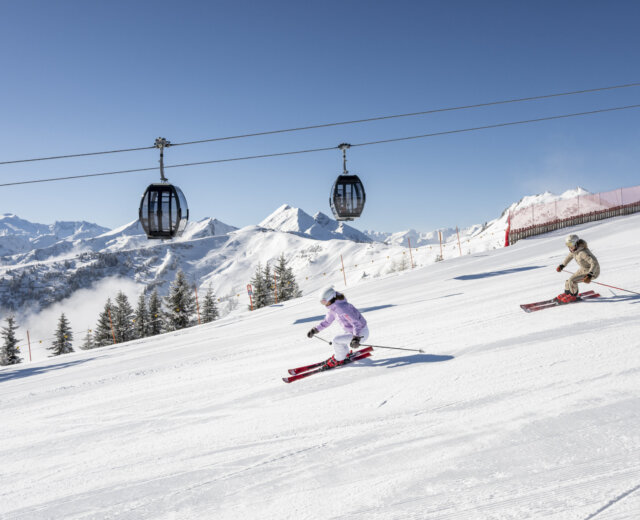 Grossarltal Ski © LorenzMasser Een skiester die aan het carven is op een perfect geprepareerde piste, met een skiliftgondel op de achtergrond en stralende zonneschijn.