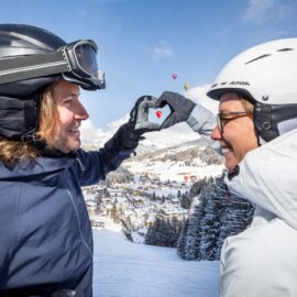 ChatGPT: Een opname van een skiër en een skiester van achteren, die elkaars hand vasthouden en samen een hart vormen – in de lucht zijn ballonnen te zien.