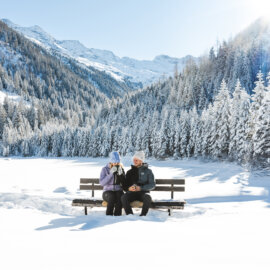 Een man en een vrouw zitten op een bankje en genieten van het uitzicht op de Hohe Tauern en het prachtige winterpanorama.