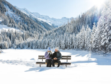 Een man en een vrouw zitten op een bankje en genieten van het uitzicht op de Hohe Tauern en het prachtige winterpanorama.