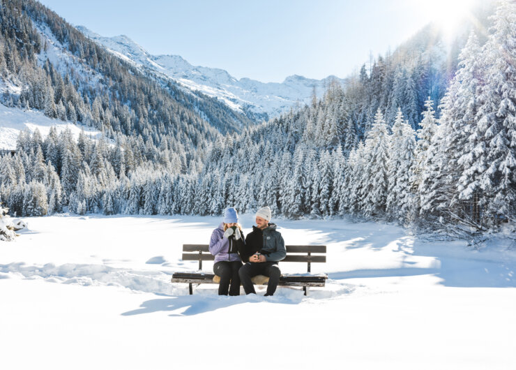 Een man en een vrouw zitten op een bankje en genieten van het uitzicht op de Hohe Tauern en het prachtige winterpanorama.