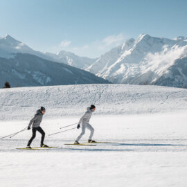 Twee langlaufers aan het skaten op de loipe op het Wasenmoos boven Mittersill, met uitzicht op de Hohe Tauern.