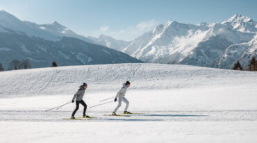 Twee langlaufers aan het skaten op de loipe op het Wasenmoos boven Mittersill, met uitzicht op de Hohe Tauern.