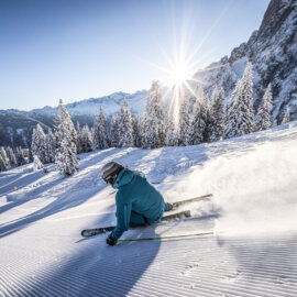 Een skiër carve de perfect geprepareerde piste af, terwijl de zon stralend schijnt.