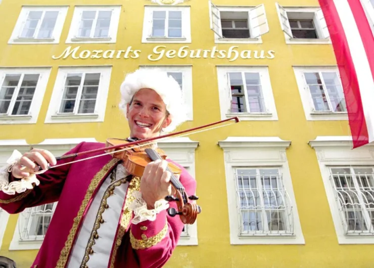 Een man in historisch kostuum speelt viool buiten Mozarts geboortehuis, een geel gebouw in Salzburg, Oostenrijk.