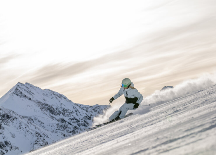 Perfecte skipiste Persoon skiet bergafwaarts op besneeuwde berg met besneeuwde toppen en een bewolkte lucht op de achtergrond.