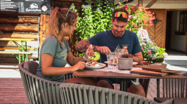 Een man en vrouw genieten samen van een maaltijd in een openluchtrestaurant met bloemen op de achtergrond.