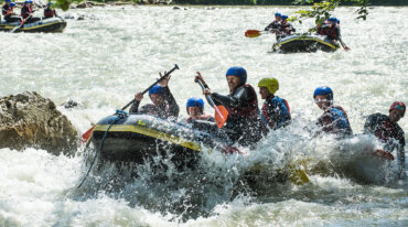 Een groep mensen met helmen raftt door stroomversnellingen en peddelt hard terwijl het water om hen heen opspat.