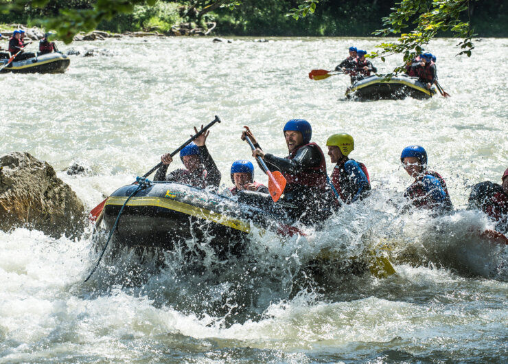 Een groep mensen met helmen raftt door stroomversnellingen en peddelt hard terwijl het water om hen heen opspat.