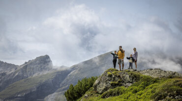 Een gezin staat op een met gras begroeide bergrug en bewondert het bewolkte, schilderachtige berglandschap in de verte.