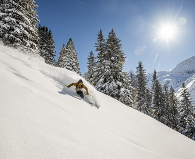 Narciarz w żółtej kurtce cieszy się świeżym śniegiem, uprawiając triki i freeskiing snowparki w słoneczny górski dzień.
