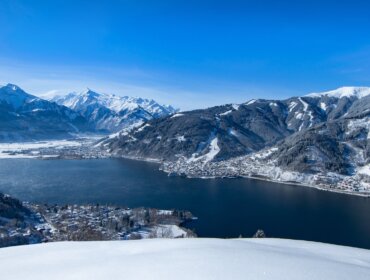 Śnieżny górski krajobraz i jezioro w pobliżu Zell am See-Kaprun, otoczone ośnieżonymi wzgórzami pod błękitnym niebem.