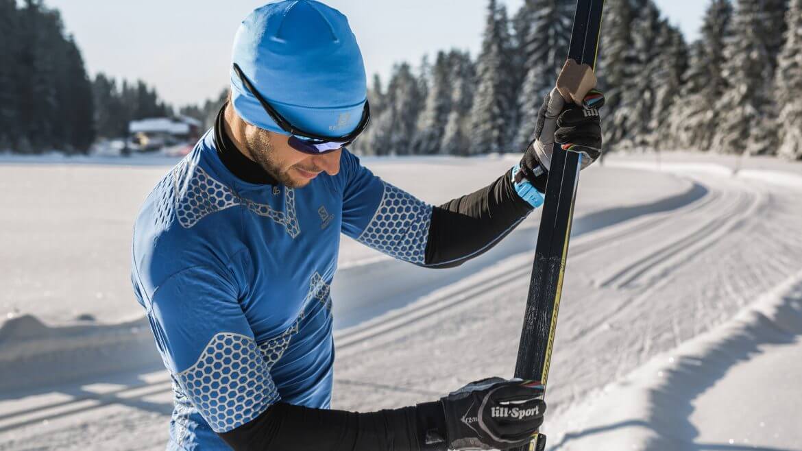 Narciarz biegowy przygotowuje sprzęt narciarski, by przypiąć go do butów i wyruszyć na świeżo przetartą trasę biegową.