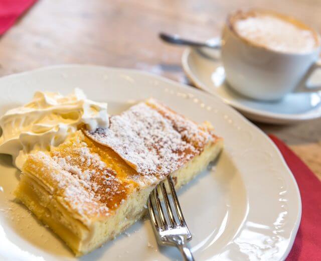 Dwa kawałki ciasta - salzburskie specjały - z bitą śmietaną i kawą, podawane z widelcem na talerzu.