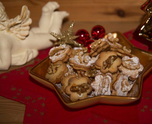 Talerz w kształcie gwiazdy z orzechowymi ciasteczkami, czerwonymi ornamentami i figurką anioła na czerwonej serwetce.