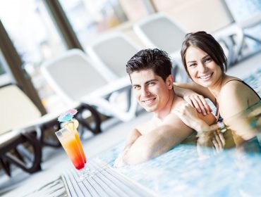 salzburger-thermen-wasserreiches-salzburgerland Uśmiechnięta para relaksująca się w basenie z kolorowym koktajlem na brzegu w pobliżu.