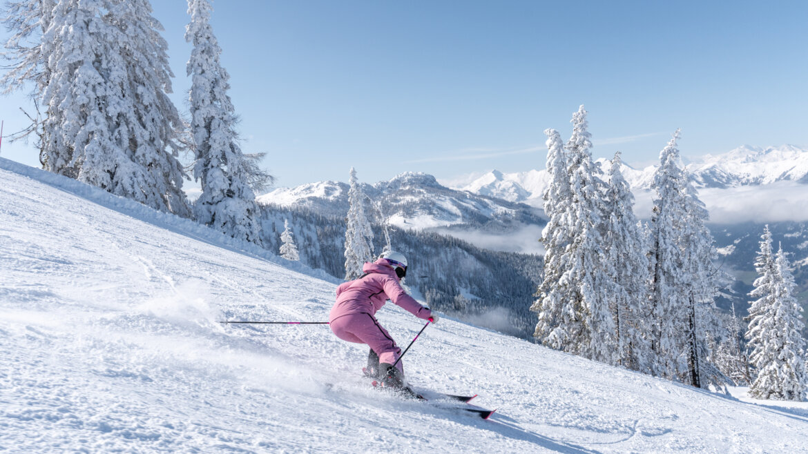 Narciarka w różowym kombinezonie narciarskim zjeżdza po stoku w St. Johann na Ziemi Salzburskiej.