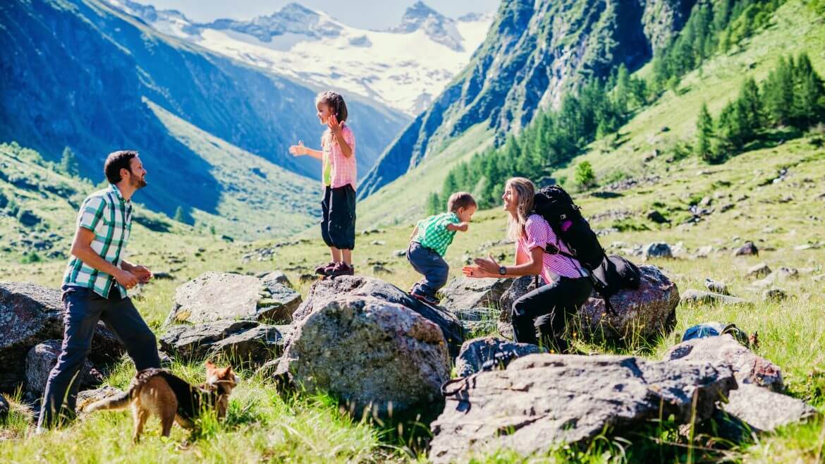 Rodzice z dwójką dzieci i psem bawią się na alpejskiej hali w Parku Narodowym, w otoczeniu trzytysięcznych szczytów Wysokich Taurów.