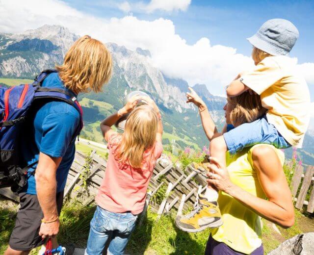 Czteroosobowa rodzina na zewnątrz, patrząca na góry; dziecko na ramionach i drugie używające lornetki.