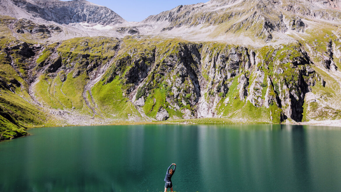 Osoba rozciągająca się w pobliżu turkusowego górskiego jeziora w malowniczej Wildkogel-Arena pod czystym błękitnym niebem.