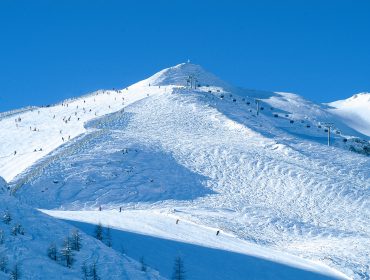 Ośnieżony stok górski z narciarzami i wyciągiem narciarskim pod czystym błękitnym niebem Zima w Salzburskim Lungau.