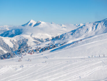 Narciarze na ośnieżonych stokach Wildkogel-Arena z odległymi szczytami pod czystym, błękitnym niebem.