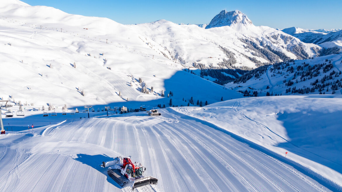 Ratrak wygładza stok narciarski w Wildkogel-Arena pod czystym, błękitnym niebem.