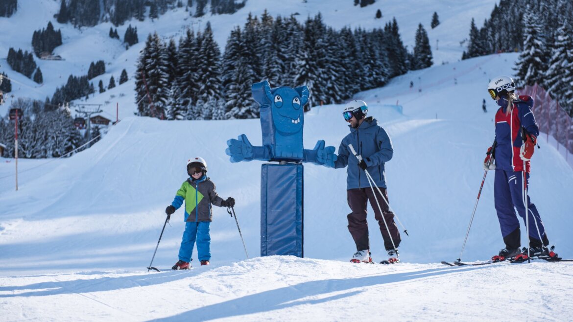Funpark Hochkönig © Hochkönig Tourismus Trzech narciarzy i niebieska maskotka cieszą się Zima w Hochkönig na zaśnieżonym stoku z sosnami i górami za plecami. (Powiększony widok)