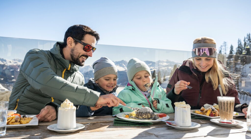 Rodzice z dwójką dzieci w kombinezonach narciarskich jedzą omlet cesarski i knedel drożdżowy.