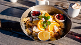 Kaiserschmarren_Hochkoenig_(c)HochkoenigTourismusGmbH Patelnia z pokrojonymi pomarańczami, dżemem i naleśnikami - idealna na Zima w Hochkönig na przytulnym drewnianym stole.