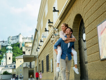Pärchen Hofstallgasse Uśmiechnięta kobieta jedzie na barana na mężczyźnie wzdłuż ulicy w pobliżu zamku podczas najważniejszej imprezy na Ziemi Salzburskiej.