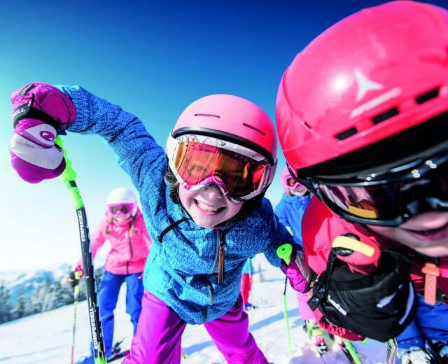 Ski Amade Dzieci w kolorowych strojach narciarskich uśmiechają się i pozują z kijkami narciarskimi podczas Zima W Ski amadé na ośnieżonej górze.