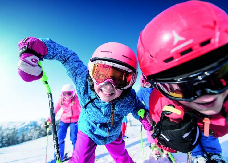 Dzieci w kolorowych strojach narciarskich uśmiechają się i pozują z kijkami narciarskimi podczas Zima W Ski amadé na ośnieżonej górze.