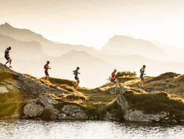 Pięć osób biegających w pobliżu jeziora o zachodzie słońca, ciesząc się latem w Obertauern z górami w tle.