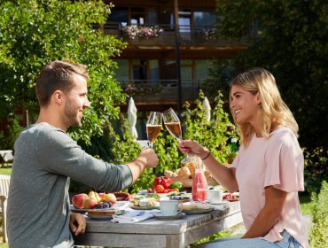 Mężczyzna i kobieta brzęczą szklankami przy stole zastawionym jedzeniem na świeżym powietrzu, delektując się posiłkiem w ogrodzie.