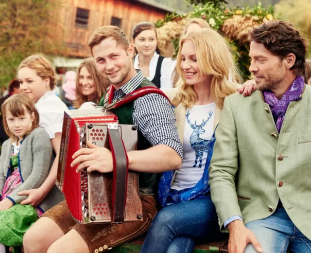 rs1253_15100-1015_bauernherbst_slt_a15_043-lpr-1170×658.jpg Muzyk z akordeonem na festynie wiejskim w otoczeniu bawiących się mieszkańców wsi i turystów.