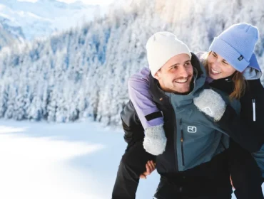 Uśmiechnięta para cieszy się przejażdżką na barana w zaśnieżonym lesie - Zima na Ziemi Salzburskiej w najlepszym wydaniu.