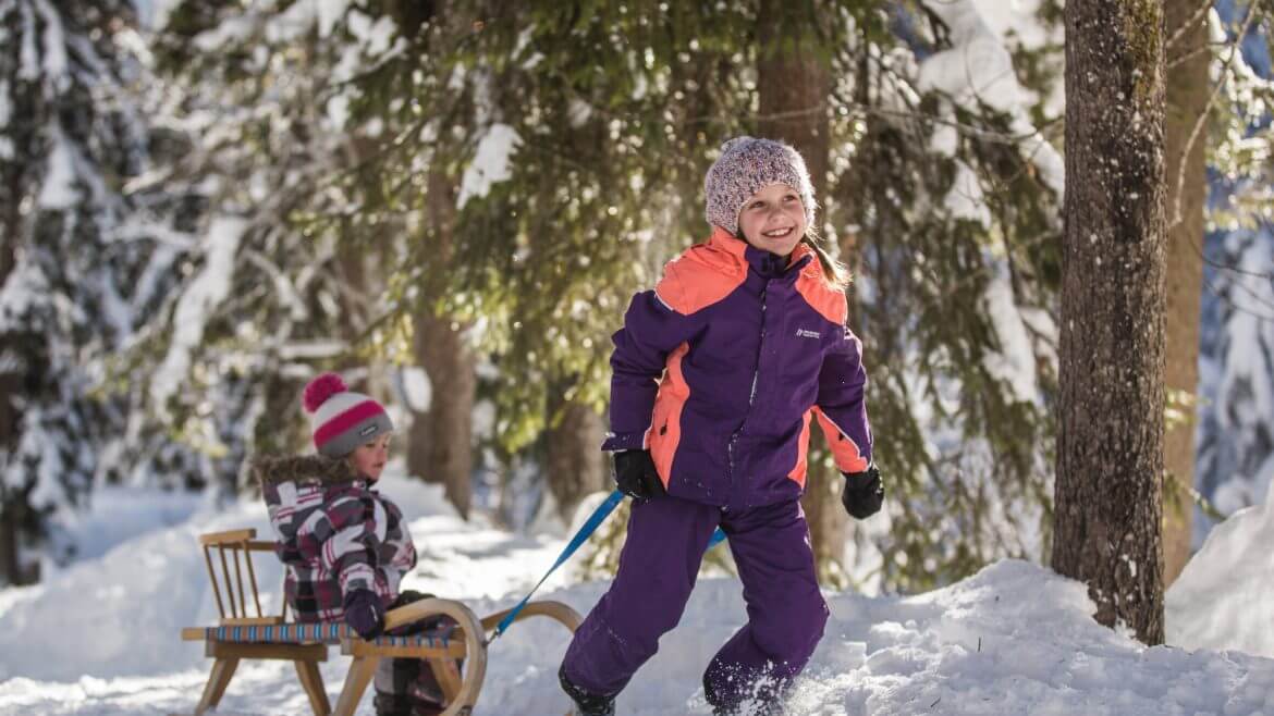 Dziewczynka ciągnąca po śniegu sanki, na których siedzi jej mały braciszek.
