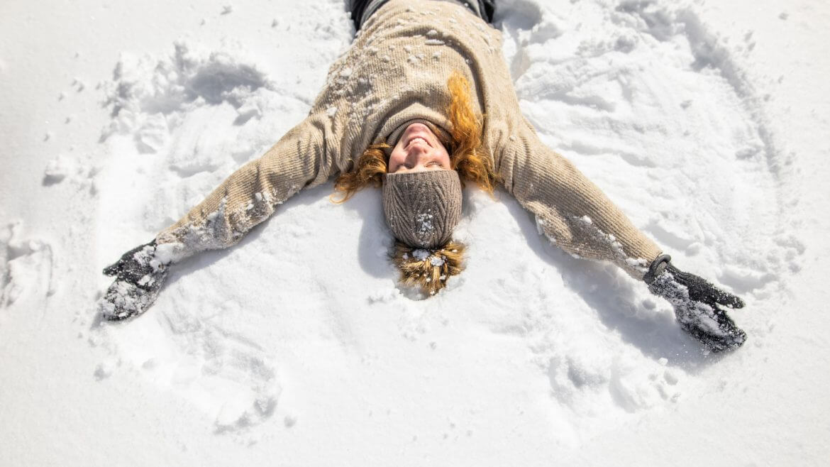 Śnieg zachęca do zabawy i dodaje nam dobrego humoru: kobieta na śniegu odciskająca w nim "śnieżnego anioła".