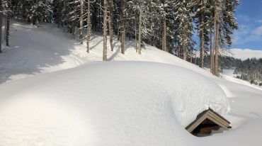 Przysypana śniegiem po dach górska chata w Pinzgau. Białe krajobrazy Ziemi Salzburskiej.