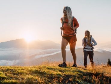 Dwie kobiety wędrujące o wschodzie słońca na trawiastym wzgórzu-Dla takich chwil żyjemy wśród gór i chmur.